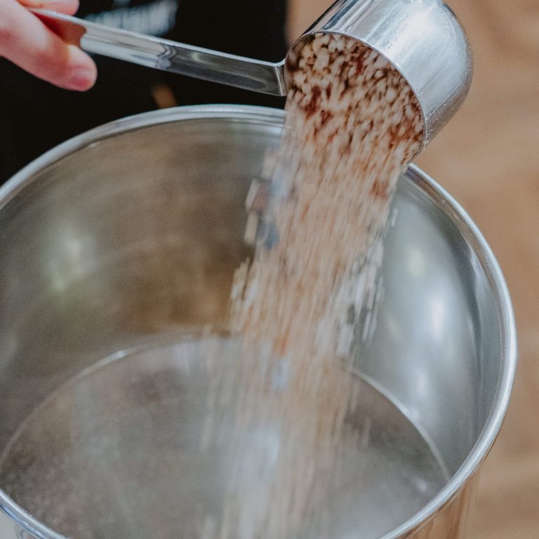 Die Nussmus-Mühle von oben wie gerade mit einem Schöpflöffel geröstete, gehackte Nüsse in den Trichter geleert werden.