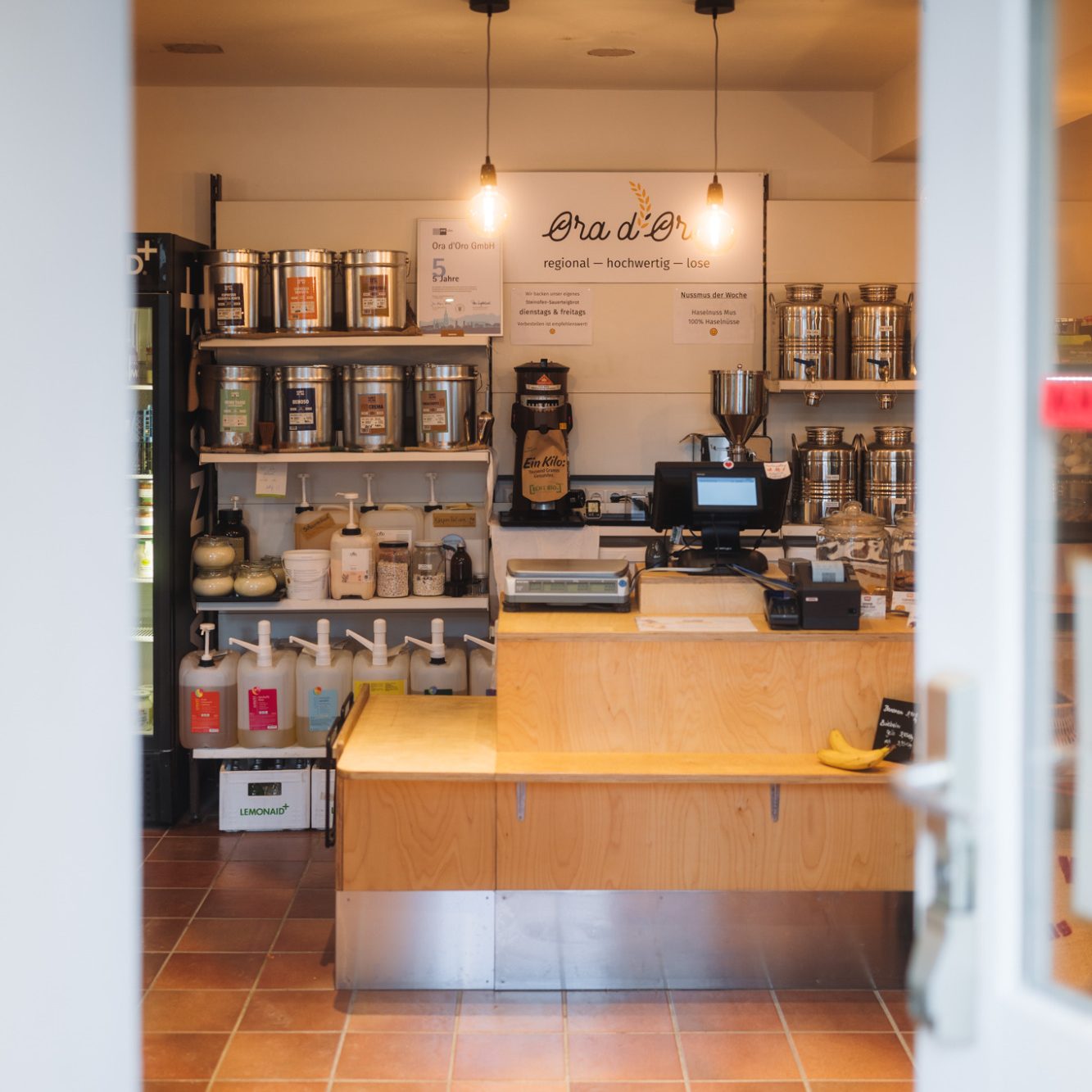 Hereinspaziert. Die Eingangstür ist geöffnet. Man sieht den Kassenbereich.